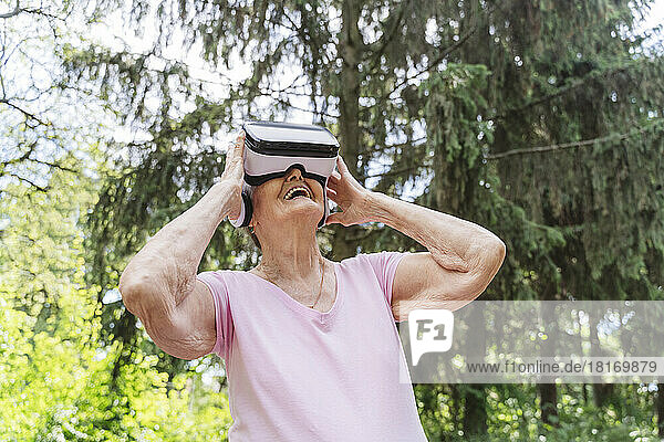 Senior woman watching through VR Goggles and laughing in public park