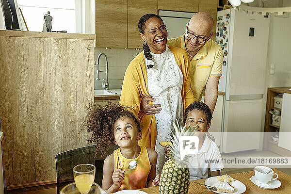 Man embracing happy woman by children at dining table