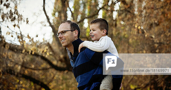 Ein Vater spielt mit seinem kleinen Sohn  der während eines Familienausflugs in einem Stadtpark im Herbst Huckepack fährt; St. Albert  Alberta  Kanada