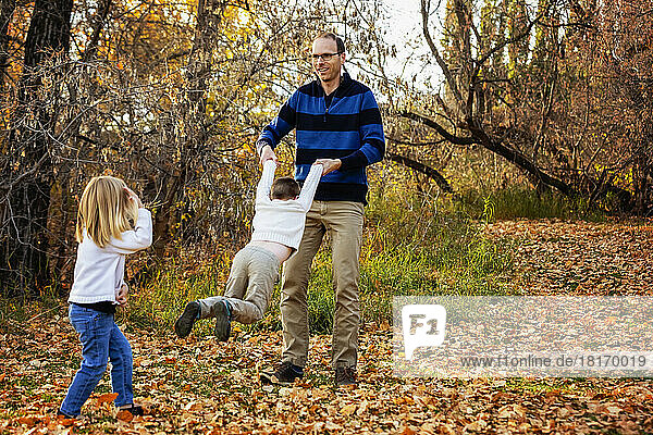 A father swinging his son around and spending quality time with his children during a family outing at a city park in the fall season; St. Albert  Alberta  Canada