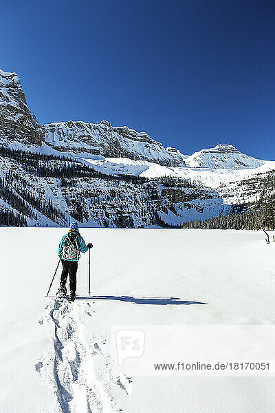 Frau beim Schneeschuhwandern auf einem unberührten schneebedeckten See mit schneebedeckten Rocky Mountains im Banff National Park; Lake Louise  Alberta  Kanada