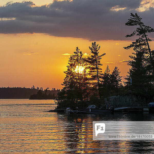 Goldener Sonnenuntergang über einem schönen See mit Motorboot und Dock entlang der Uferlinie  Lake of the Woods  Ontario; Ontario  Kanada
