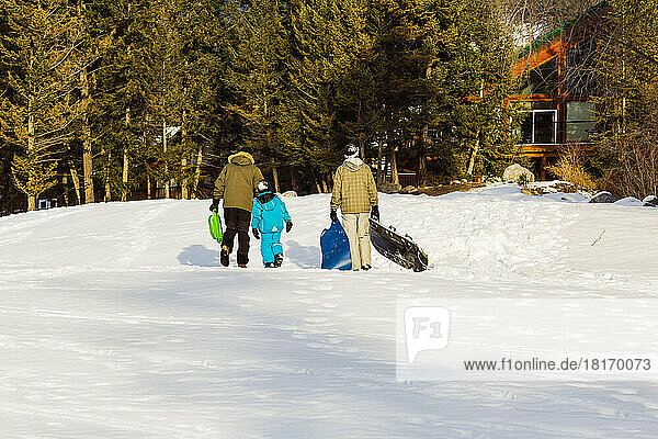 Zwei Männer gehen mit einem Kind spazieren  nachdem sie in einem Bergdorf gerodelt sind; Fairmont Hot Springs  British Columbia  Kanada