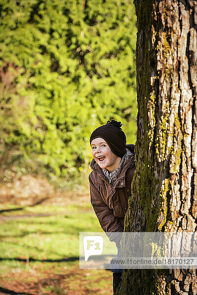 Ein kleiner Junge lugt mit einem breiten Lächeln hinter einem Baum hervor; Langley  British Columbia  Kanada