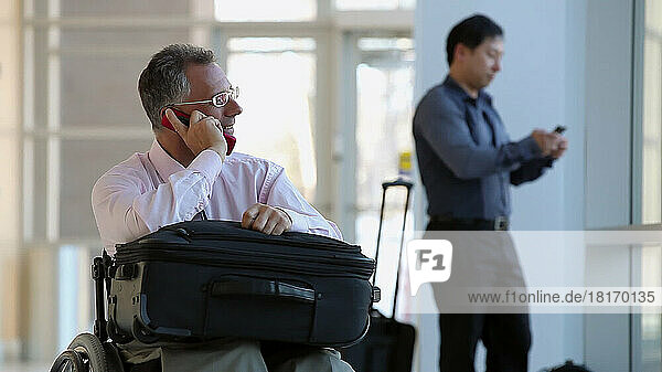 Mann mit Rückenmarksverletzung in einem Rollstuhl auf einem Flughafen  während ein Passagier vorbeifährt; Massachusetts  Vereinigte Staaten von Amerika