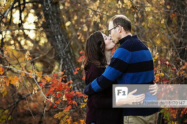 Mature married couple stand kissing while spending quality time together outdoors in a city park during the fall season; St. Albert  Alberta  Canada