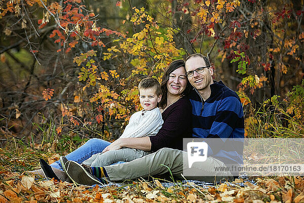 A mother and father spending some qualtiy time together with their son and looking at the camera during a family outing in a city park during the fall season; St. Albert  Alberta  Canada