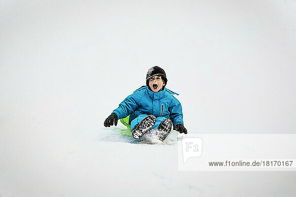 Young Boy Riding Down A Snowy Hill On A Green Plastic Sled At A Mountain Resort; Fairmont Hot Springs  British Columbia  Canada