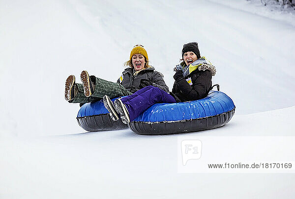 Two women tubing in tandem down a ski hill; Fairmont Hot Springs  British Columbia  Canada