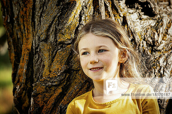 Young girl playing near a tree and pausing for a moment in a city park on a warm fall afternoon; St. Albert  Alberta  Canada