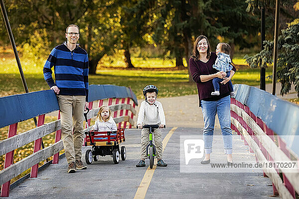 Portrait of a young family on a bridge over a river in a city park during the fall season and their baby daughter has Down Syndrome; St. Albert  Alberta  Canada