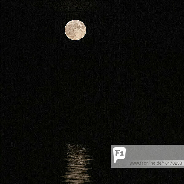 Full moon glowing in a black sky  illuminated view of the near side of the moon  reflected in water; Ontario  Canada