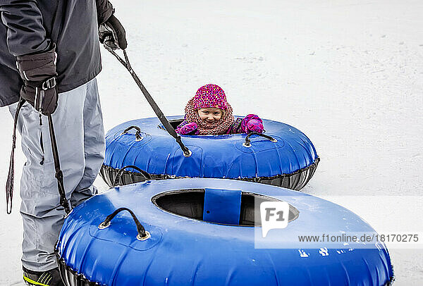 A father and his young daughter getting ready to go tubing down a ski hill together; Fairmont Hot Springs,  British Columbia,  Canada