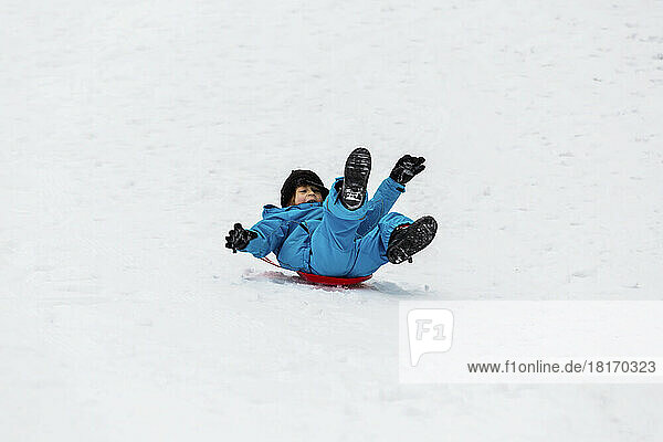 Young Boy Riding Down A Snowy Hill On A Blue Plastic Sled At A Mountain Resort; Fairmont Hot Springs  British Columbia  Canada