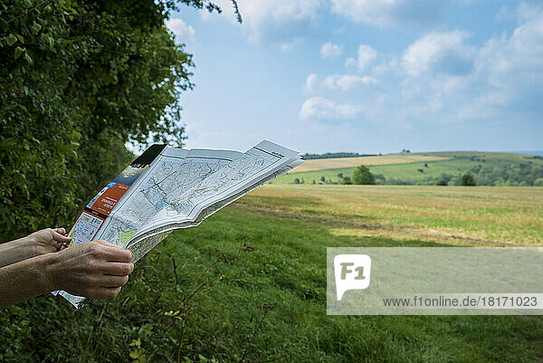 Hände halten eine Karte am Rande eines Feldes mit Blick auf die weite englische Landschaft; Rockbourne  Wiltshire  England