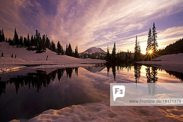Mirror image of Mount Rainier and forest reflected in Tipsoo Lake at sunset with a sunburst shining through trees  Mount Rainier National Park; Washington  United States of America