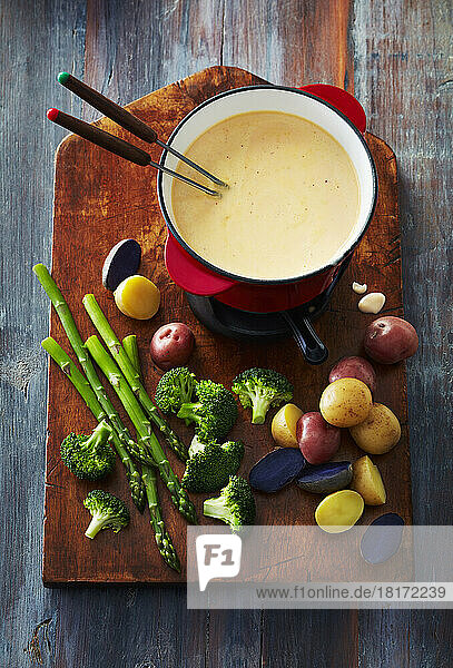 Cheese fondue with vegetables for dipping on a wooden cutting board