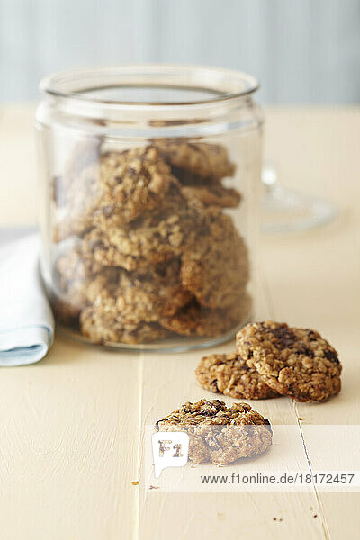 Oatmeal cookies in a glass cookie jar on a cream colored wood surface