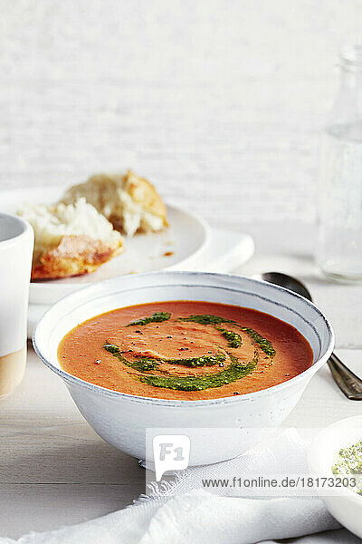 Tomato soup with pesto and a side of crusty bread in the background