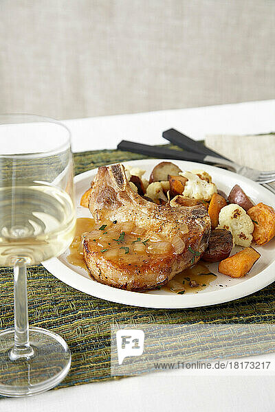 Pork chop with mixed vegetables on white plate with white wine