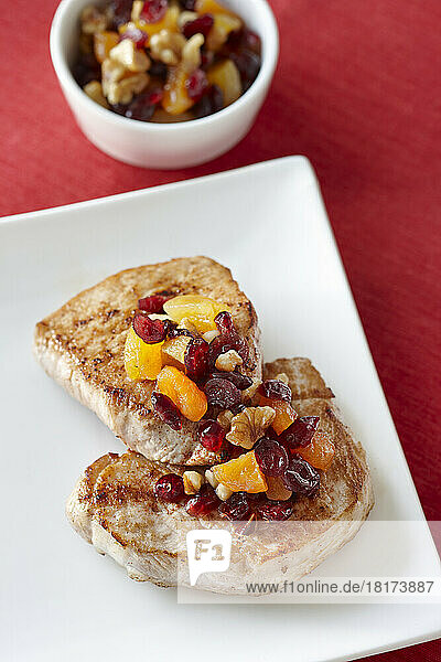 Porkchops on Plate dressed with Cranberries  Walnuts  and Dried Apricots  Bowl of extra Dressing in the background