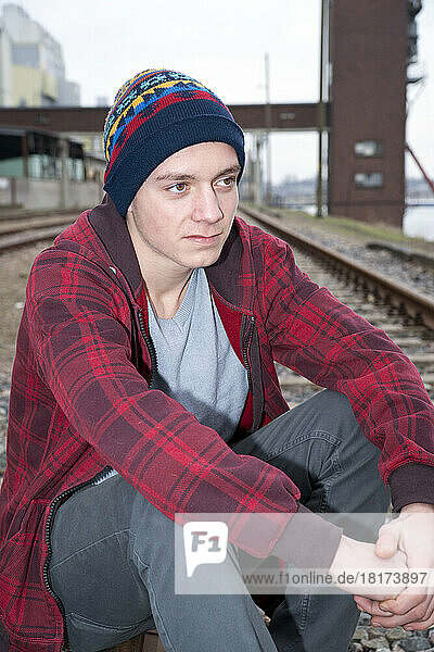 Close-up portrait of teenage boy sitting on railroad tracks near harbour  Germany