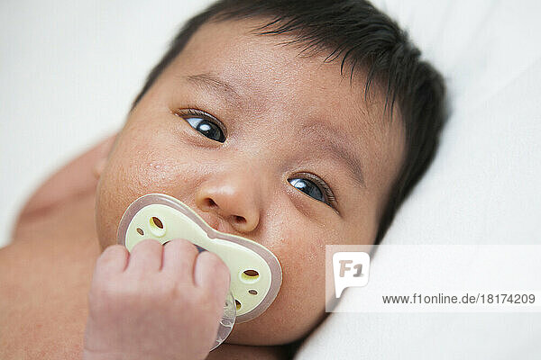 Close-up portrait of newborn Asian baby with baby acne using pacifier  studio shot on white background