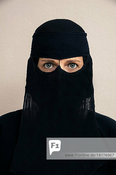 Close-up portrait of woman wearing black muslim hijab and muslim dress  looking at camera  studio shot on white background