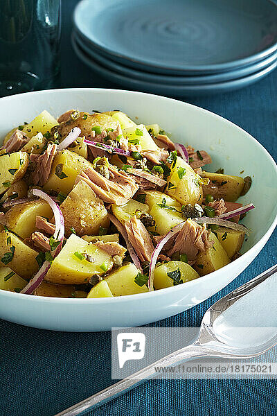 Potato salad with tuna  capers and purple onions on a teal background