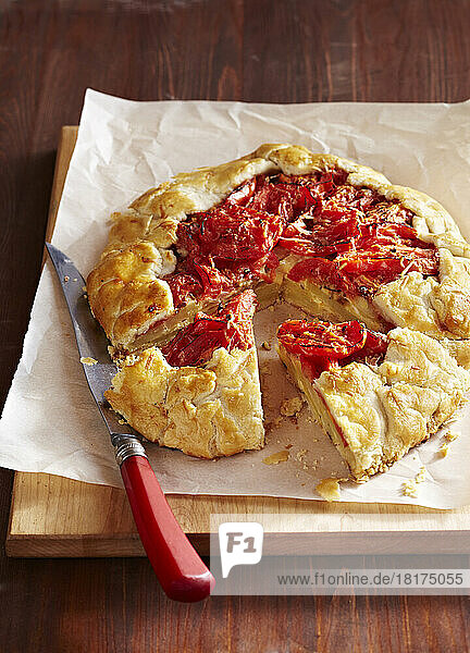 Tomato and potato galette on a cutting board with a knife and parchment paper