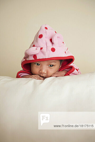 Portrait of two week old  newborn Asian baby girl in pink polka dot hooded jacket  studio shot on white background