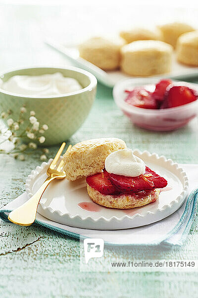 Scones with strawberries and whipped cream on a fancy white plate