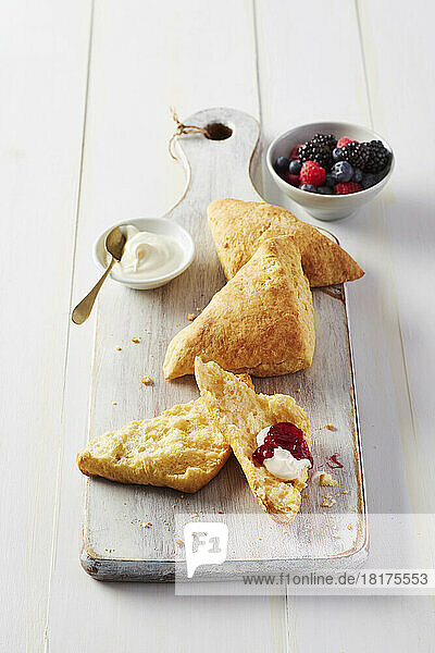 Fresh scones on a cutting board with clooted cream and side dish of berry