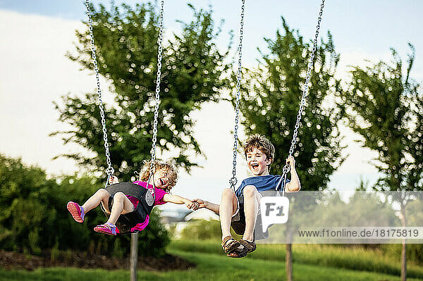 Young girl and boy holding hands while playing on a swing set at a playground; St. Albert  Alberta  Canada