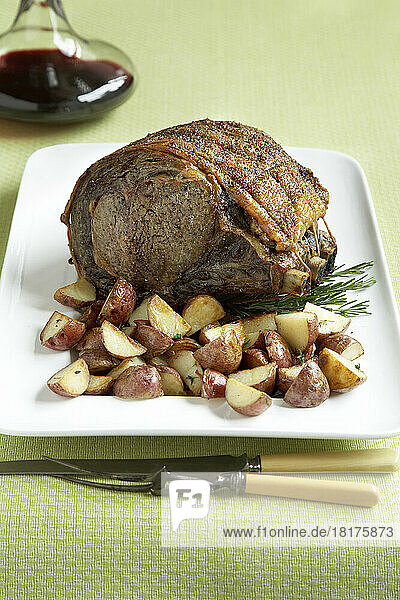 Prime rib roast beef with baby red potatoes & red wine on a green background