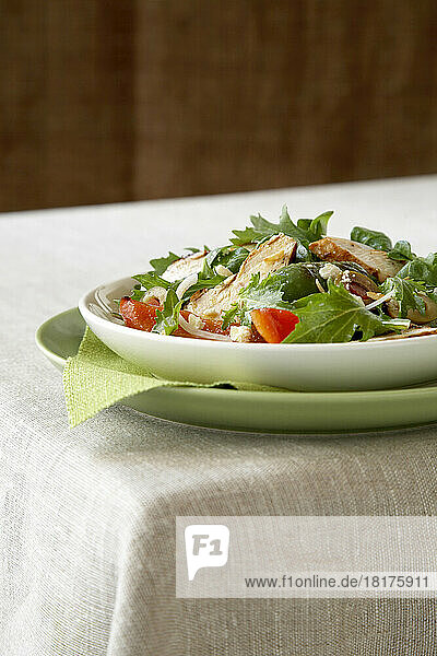 Grilled chicken salad with tomatoes and leafy greens in shallow bowl