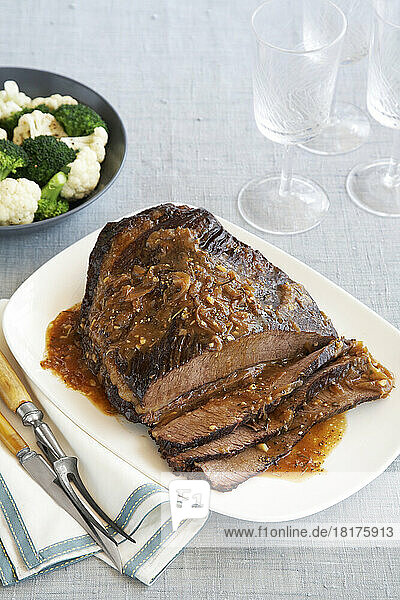 Beef brisket on platter with a side dish of cauliflower and broccoli