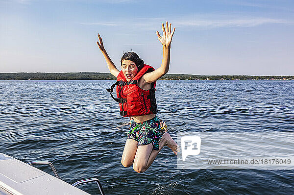 Young boy jumping off a boat and swimming in a lake with a lifejacket  Lac Ste. Anne; Alberta Beach  Alberta  Canada