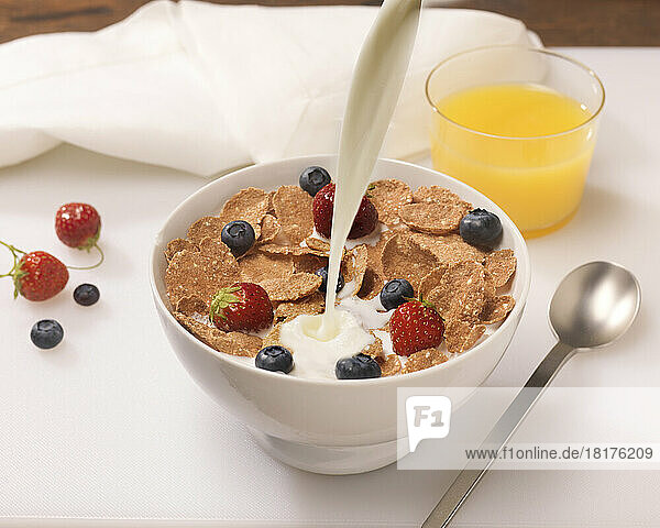 Milk Pouring in Bowl of Cereal Flakes with Berries and Orange Juice