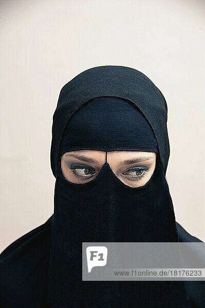 Close-up portrait of young woman wearing black  muslim hijab and muslim dress  eyes looking to the side showing eye makeup  studio shot on white background