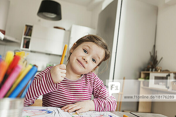 Girl sitting at Table Colouring Pictures and Smiling at Camera