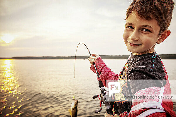 Young boy catching a fish on a rod from a boat on Lac Ste. Anne at sunset; Alberta Beach  Alberta  Canada