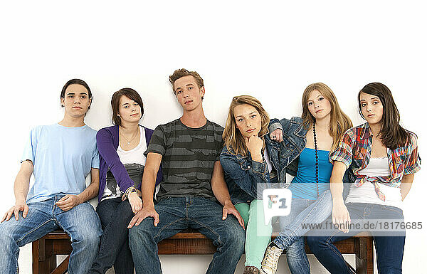 Portrait of six young people sitting together on a bench  studio shot on white background