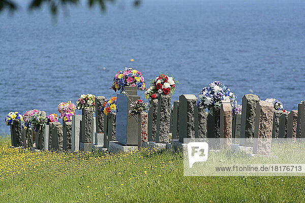Grave stones with bouquets in a seaside Catholic cemetery on the Gaspesie.; Parc de la Gaspesie  Quebec  Canada.