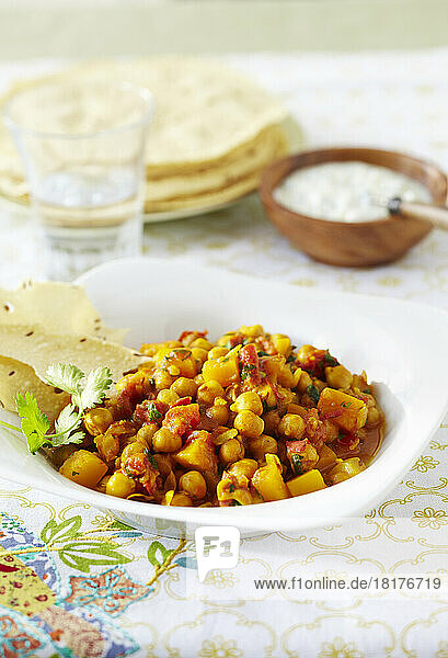 Bowl of chickpea curry with papadum and raita