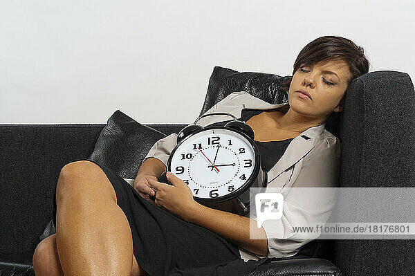 Portrait of Mid-Adult Woman Sleeping on Sofa and holding Alarm Clock