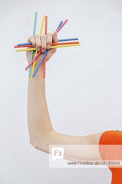 Hand of woman holding colored pencils in front of white wall