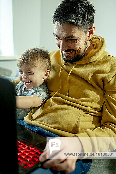Glücklicher Vater sitzt mit Sohn und schaut auf Laptop