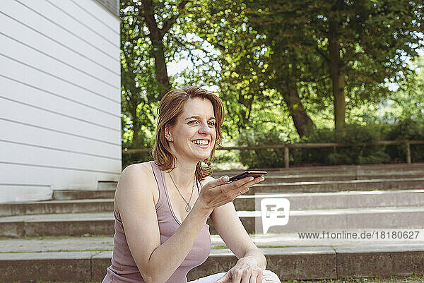 Happy woman talking on speaker phone sitting on steps in park