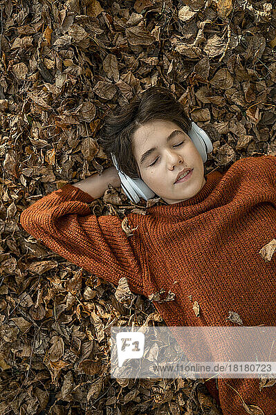 Junge mit geschlossenen Augen hört Musik über drahtlose Kopfhörer  die auf trockenen Blättern liegen